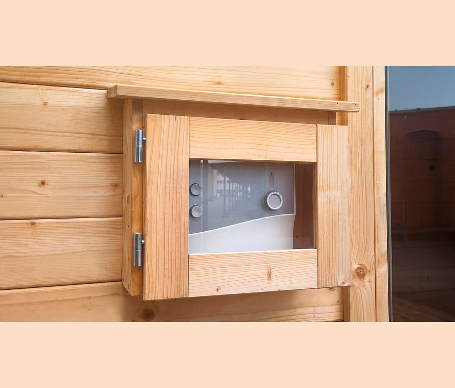 Nahaufnahme einer hellen Holzwand mit einem offenen Holzrahmen, der ein grau-weißes Bedienfeld zeigt. Das Bedienfeld hat eine transparente Abdeckung, zwei runde Knöpfe und einen größeren Drehregler.