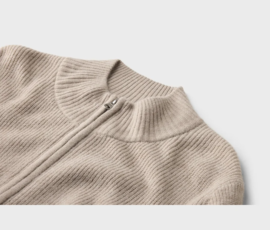 Nahaufnahme eines beigen gerippten Strickpullovers mit Stehkragen und silbernem Reißverschluss.