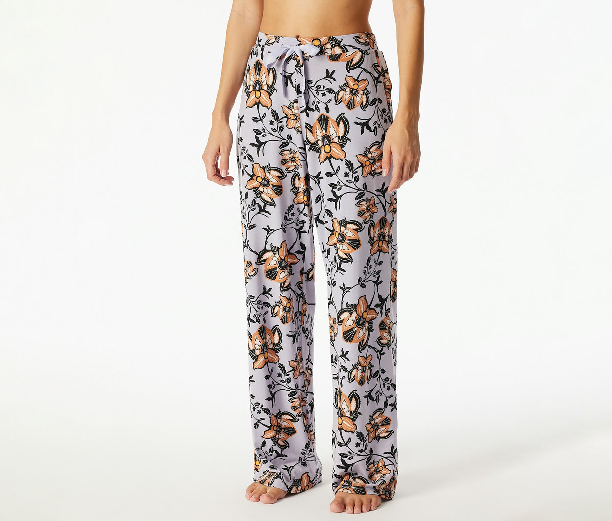 Eine Person trägt hellviolette Pyjamahosen mit orangefarbenem und schwarzem Blumenmuster, die an der Taille mit einem Kordelzug gebunden sind.