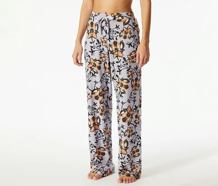 Eine Person trägt hellviolette Pyjamahosen mit orangefarbenem und schwarzem Blumenmuster, die an der Taille mit einem Kordelzug gebunden sind.