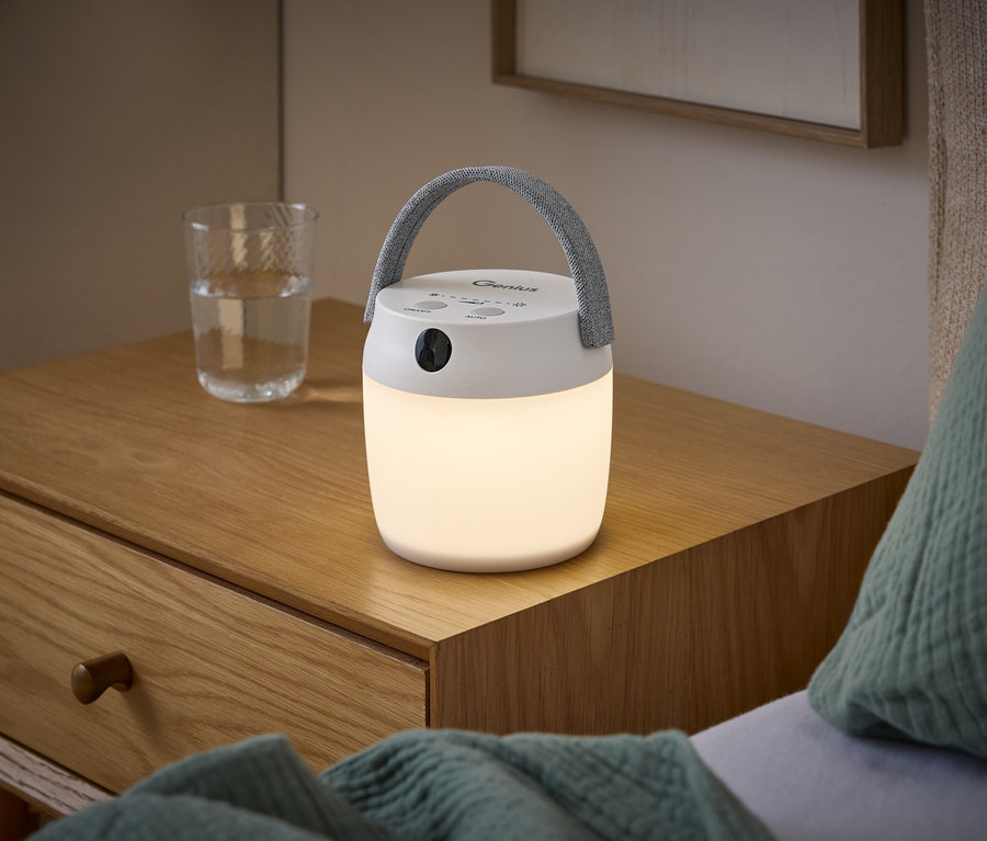 Eine leuchtende LED-Multifunktionsleuchte mit Bewegungssensor und grauem Griff steht auf einem Holznachttisch neben einem Wasserglas.