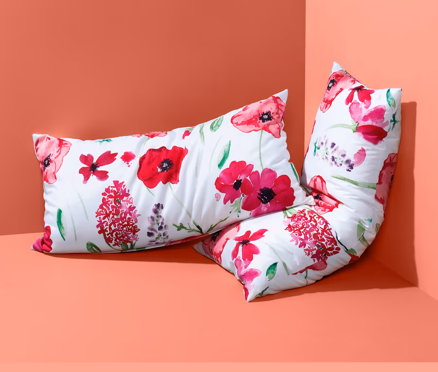 Zwei Renforcé-Kopfkissenbezüge mit Blumenmuster liegen in einer Ecke.