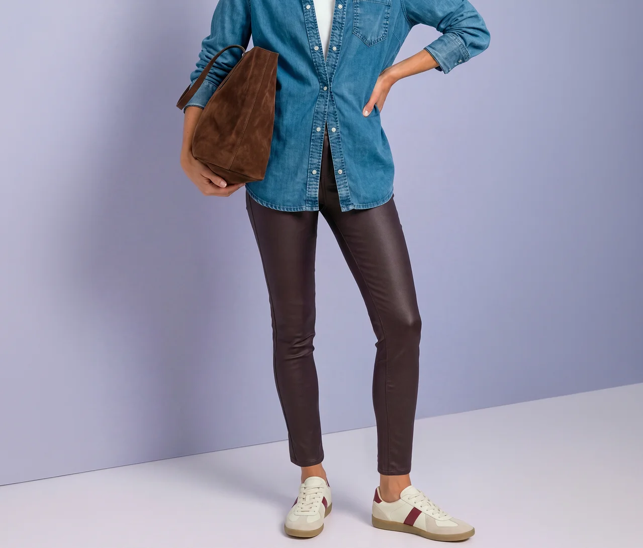 Person in blauem Jeanshemd, roter Street One Hose in Lederoptik und weißen Sneakers mit bordeauxrotem Streifen, eine braune Tasche haltend.
