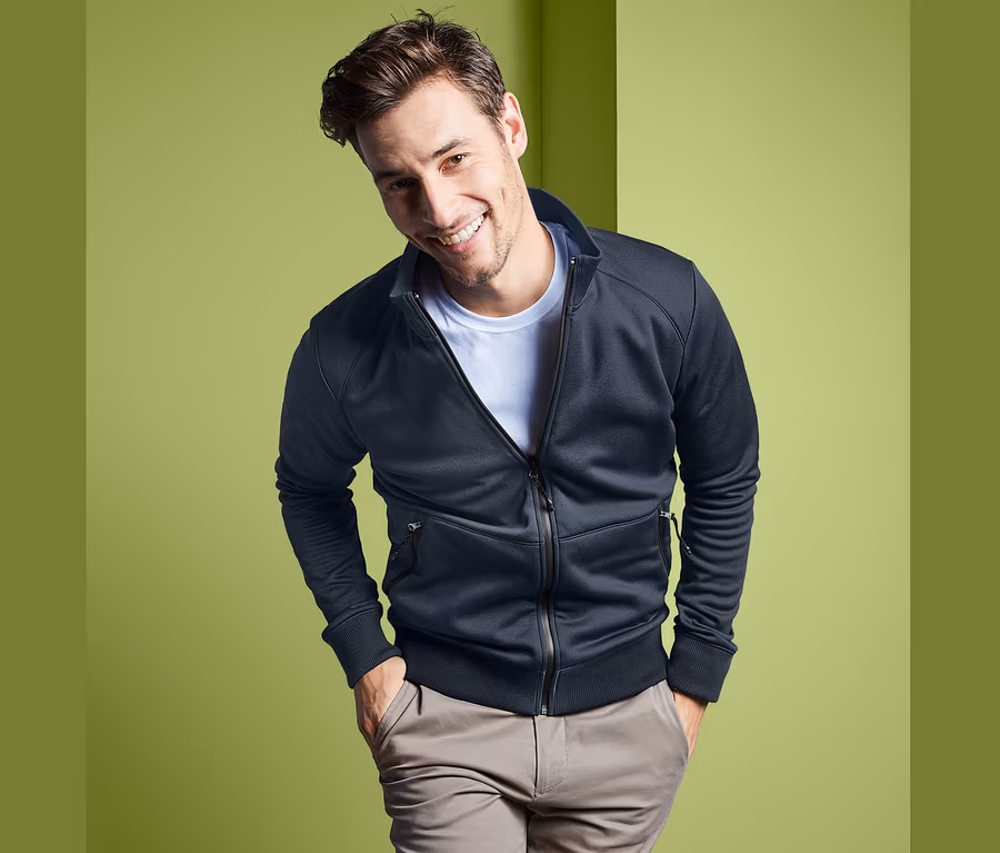 Mann lächelt und posiert in einer schwarzen Funktions-Sweatjacke mit Reißverschluss.