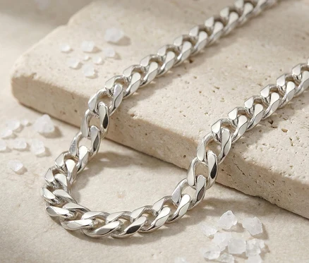 Ein Amor 925 Silber Panzer-Armschmuck liegt auf einer hellbeigen, strukturierten Steinoberfläche. Weiße, kristallartige Stücke sind um den Schmuck verstreut.