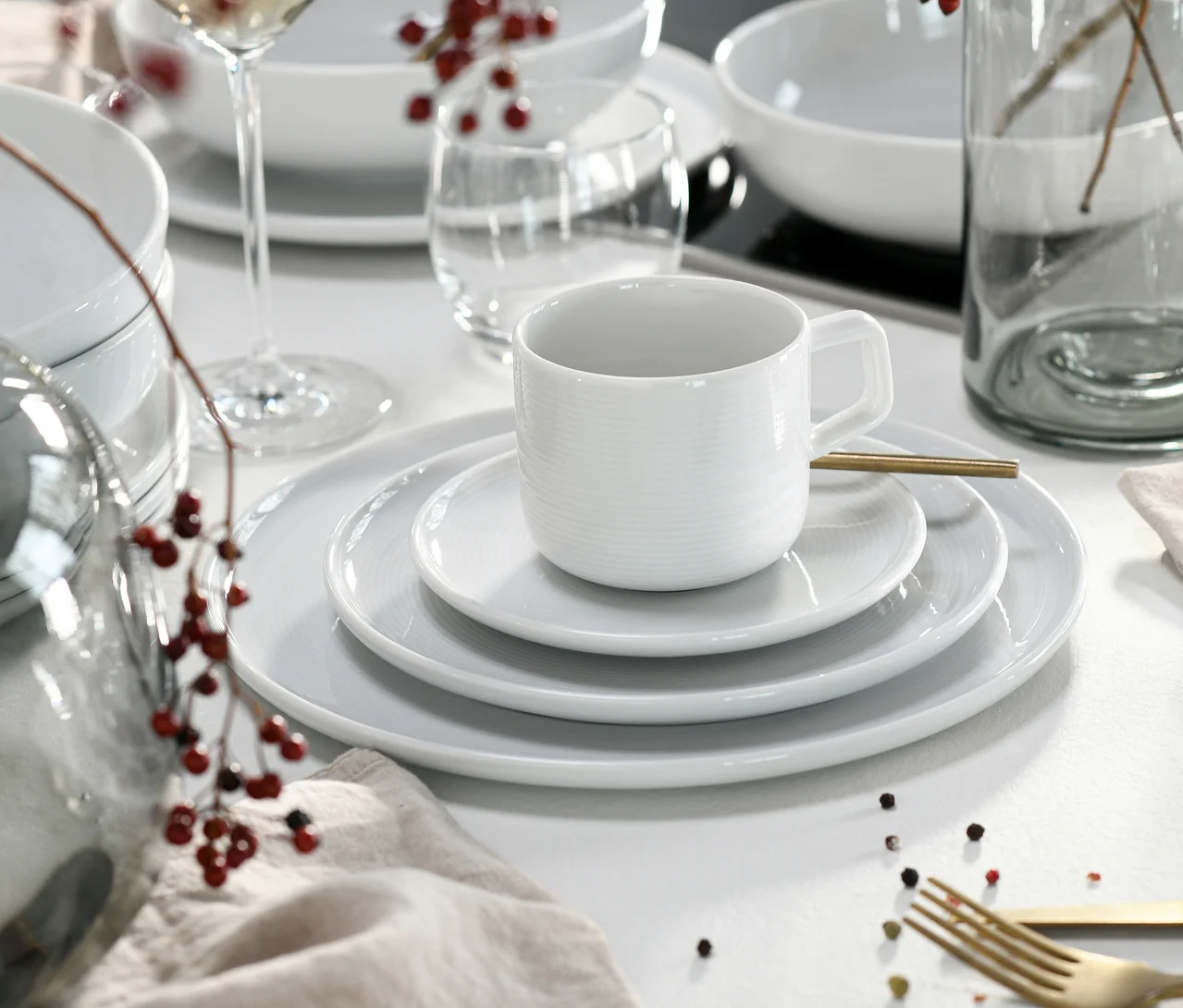 Gedeckter Tisch mit weissem, geripptem creaTable Service »Session White«: Tasse, Untertasse, gestapelte Teller, Weingläser, rote Beeren, goldenes Besteck und Leinen-Serviette.
