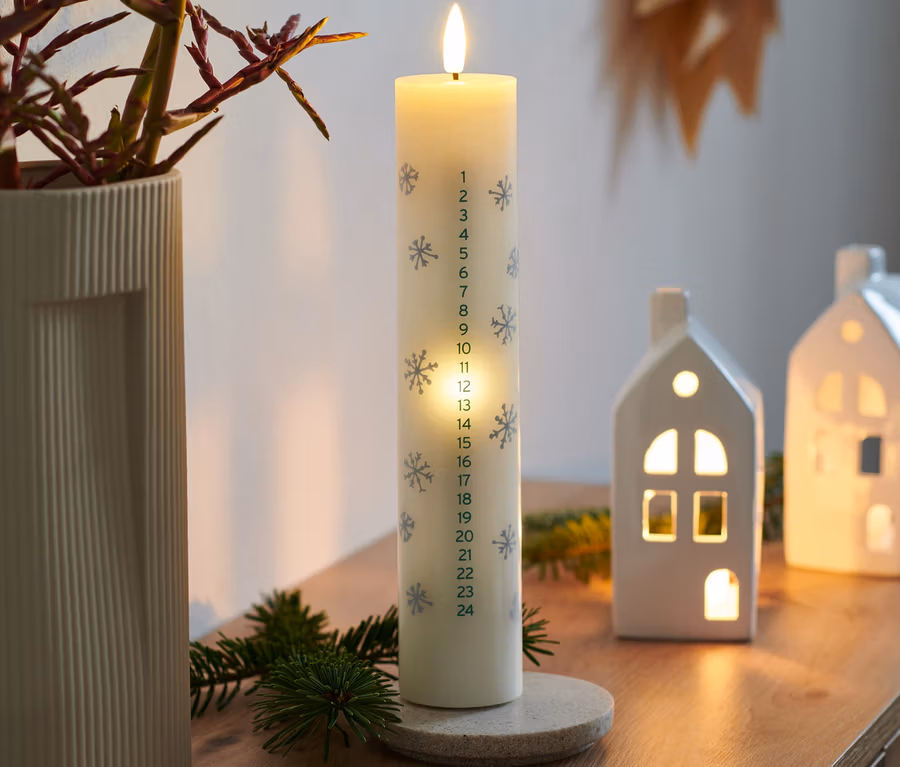 Eine brennende LED-Echtwachs-Adventskalenderkerze steht auf einem Holztisch.