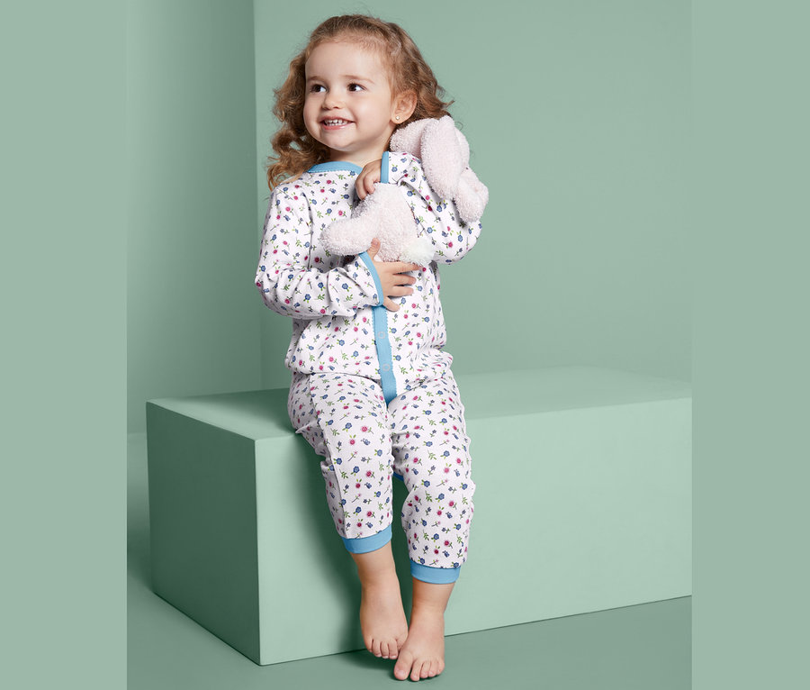 Ein Mädchen sitzt auf einem Block und umarmt ein Stoffkaninchen. Sie trägt 2 Schlafanzüge.
