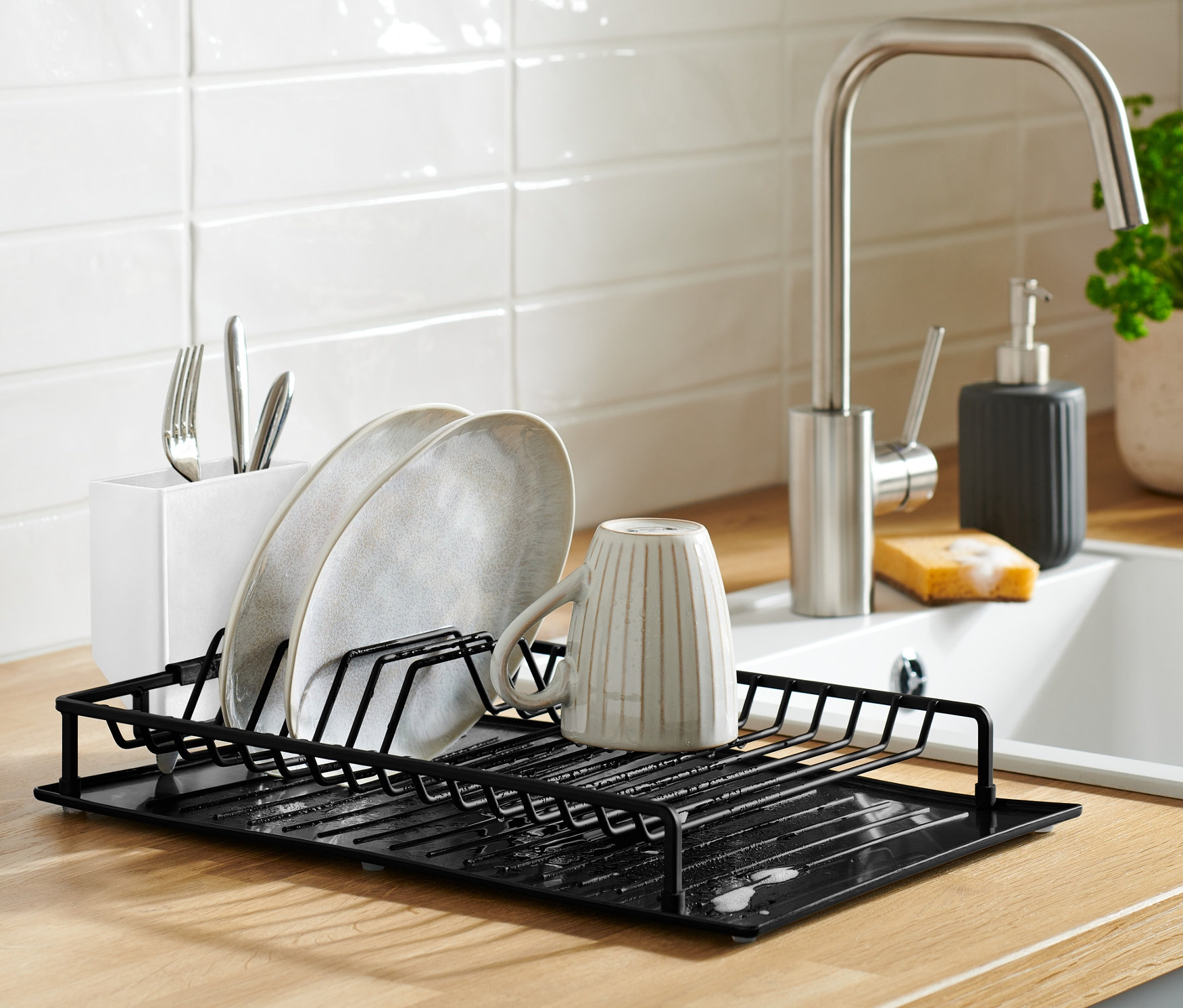Schwarzes Abtropfgestell mit Abtropfmatte auf einer Küchentheke mit Geschirr.