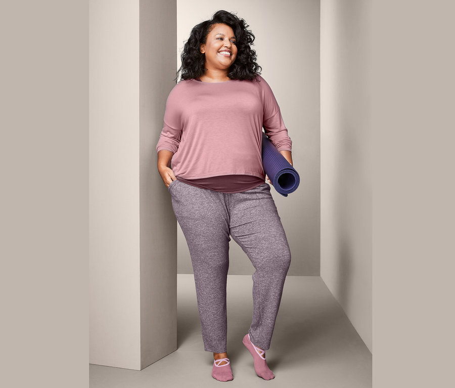 Frau hält eine zusammengerollte Trainingsmatte, trägt ein 2-in-1-Sportshirt und eine Relaxhose.