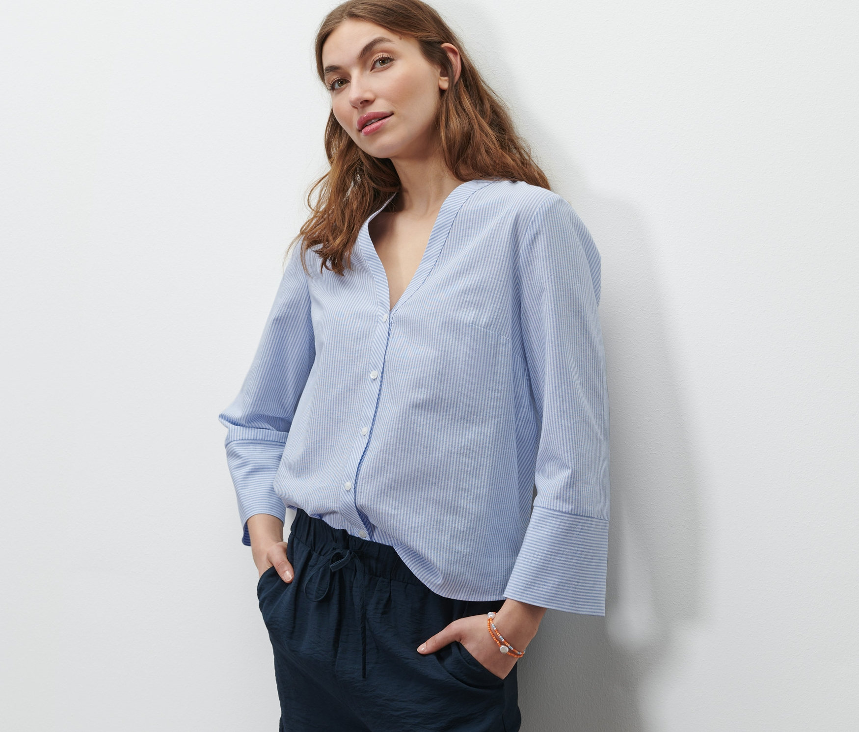 Frau steht mit Händen in den Taschen ihrer marineblauen Shorts. Sie trägt eine hellblau-weiße gestreifte Bluse.