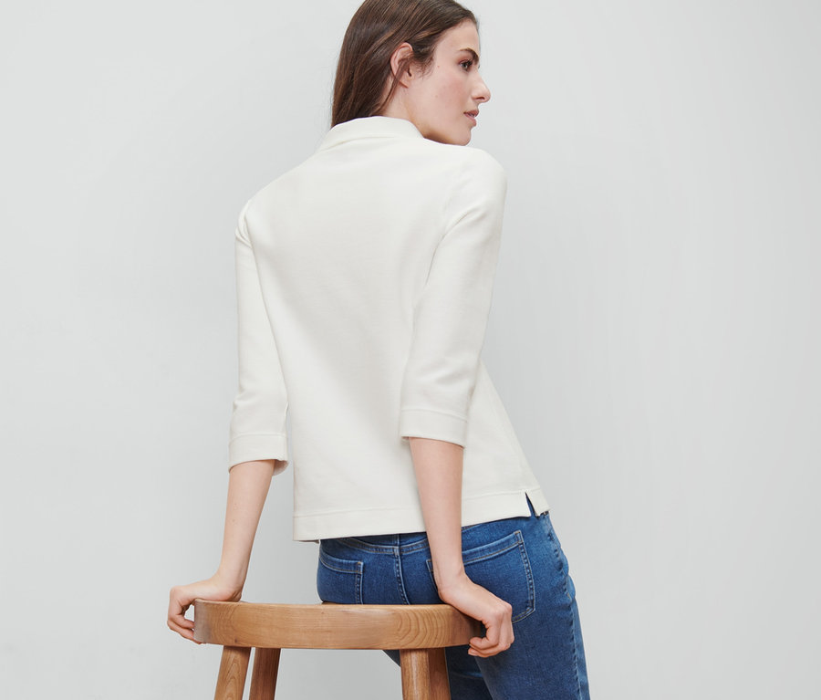 Frau sitzt auf einem Holzhocker und trägt ein cremefarbenes Sweatshirt mit 3/4-Arm.