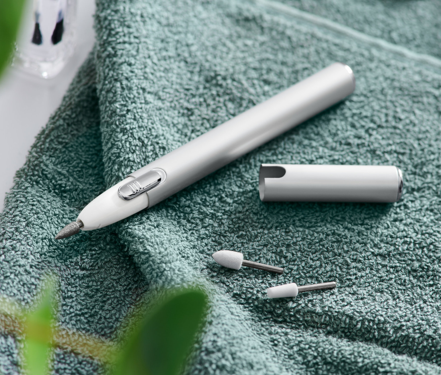 Ein Maniküre-Pediküre-Gerät liegt auf einem grünen Handtuch neben Aufsätzen, einer Feile und einer Schere.