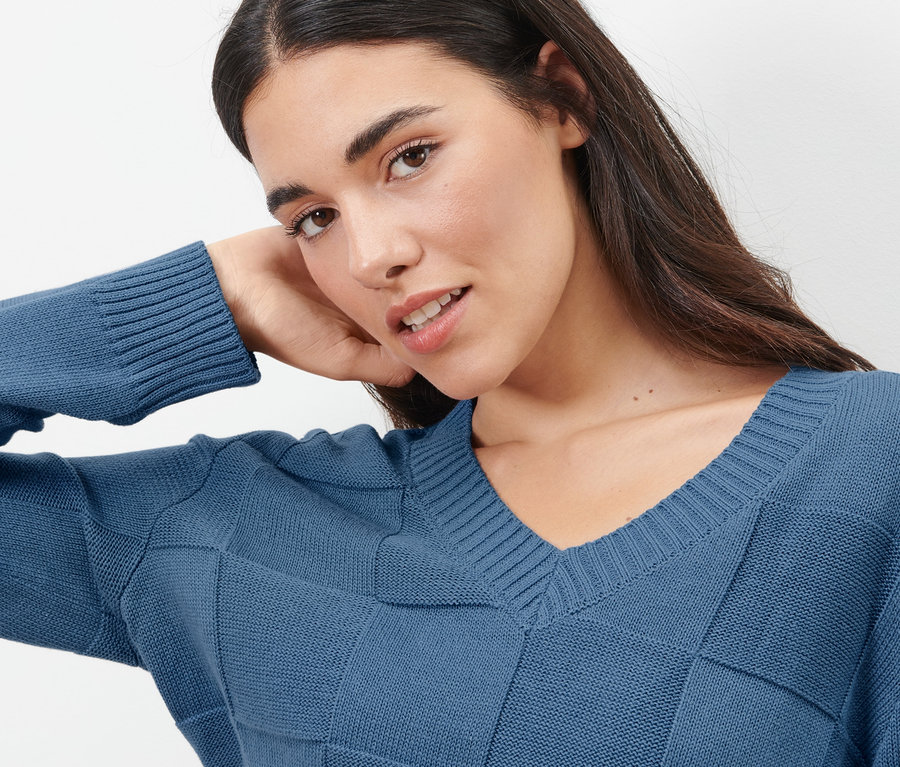 Frau posiert in blauem Pullover mit Karostruktur.
