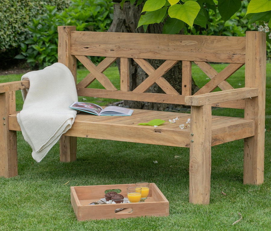 DeVries Gartenbank aus Holz mit Decke, offenem Buch und einem Tablett mit Getränken und Muffins auf dem Rasen.
