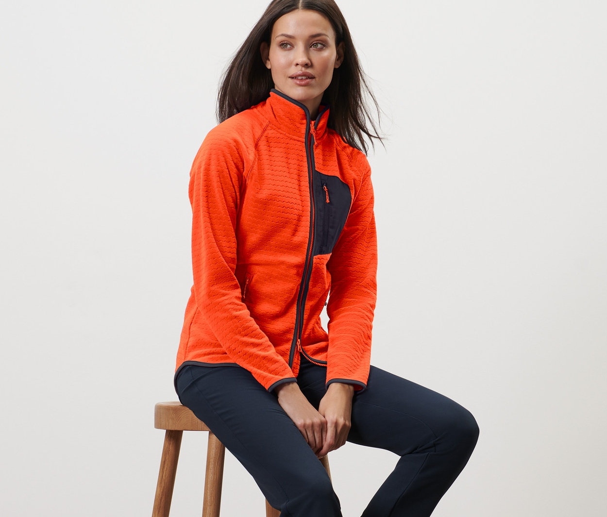 Frau sitzt auf einem Hocker und trägt eine Fleecejacke.