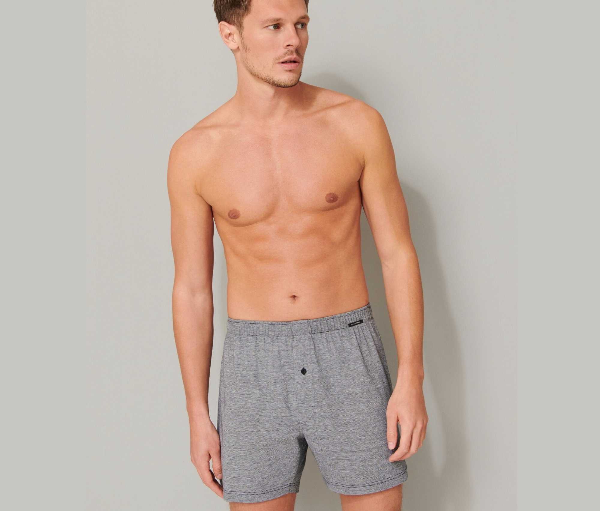 Mann mit freiem Oberkörper posiert in hellgrauen 2 SCHIESSER Boxershorts aus Baumwolle.