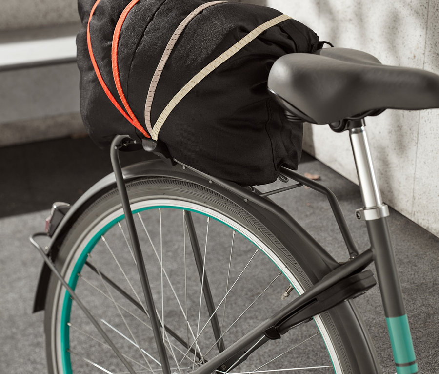 Ein Fahrrad-Spanngurt sichert eine schwarze Tasche auf dem Gepäckträger eines Fahrrads.