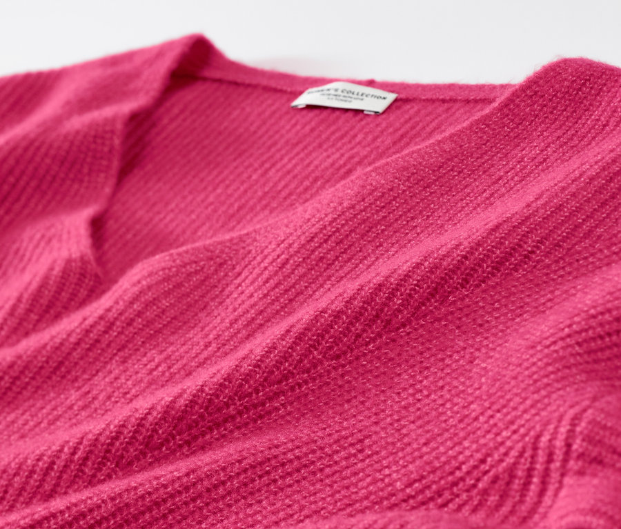 Detailaufnahme eines himbeerfarbenen Grobstrickpullovers.