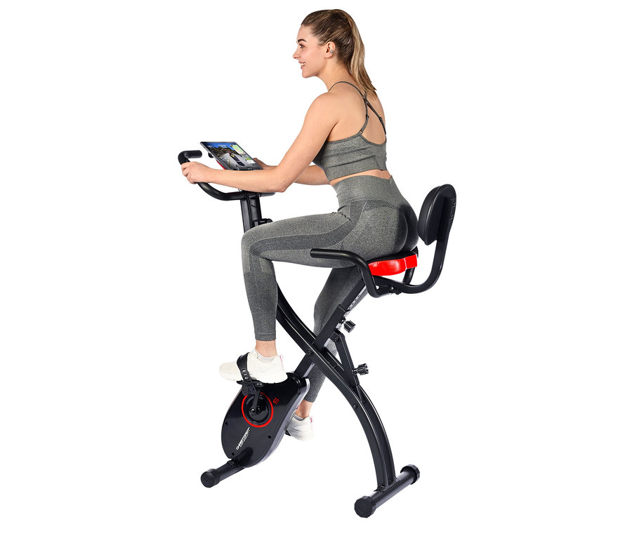 Frau trainiert auf S-Bike, trägt Sportkleidung und schaut auf ein Tablet.