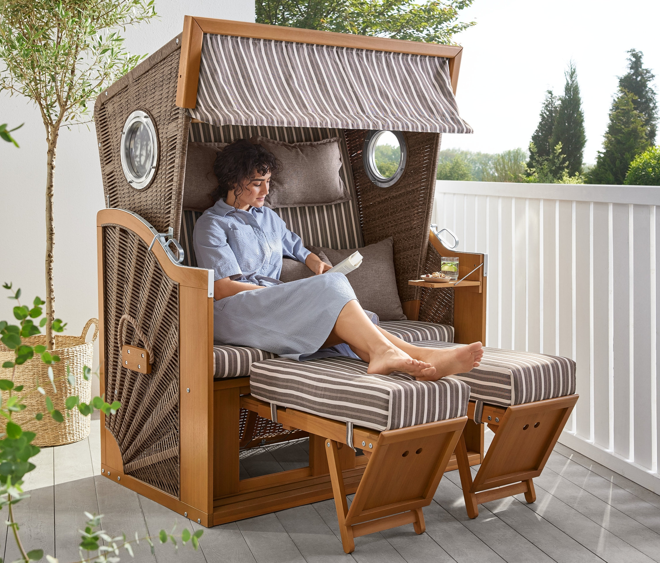 Frau sitzt im Premium-Strandkorb XL mit Ausklapptisch und liest.
