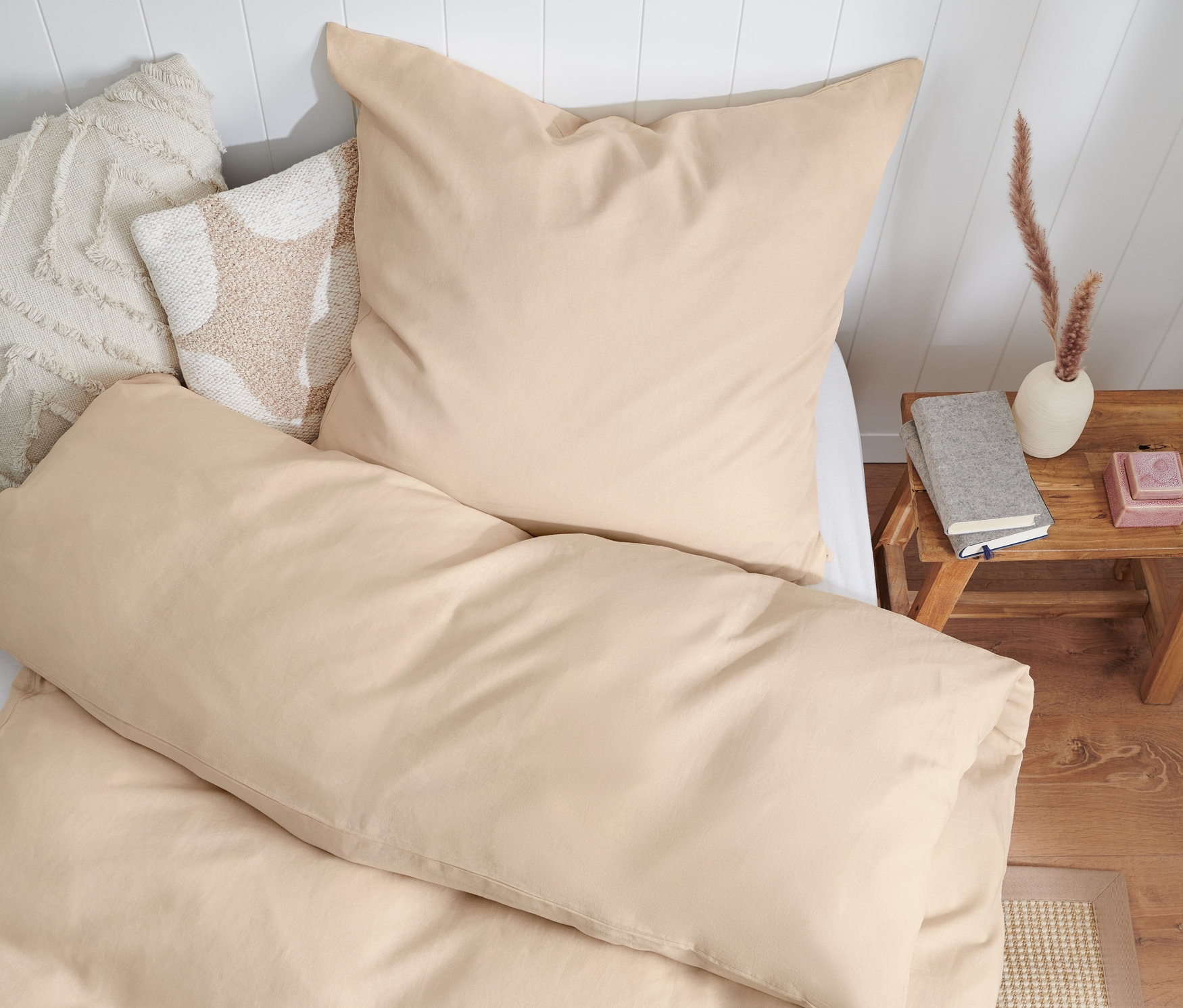 Beige Bettwäsche aus gewaschenem Leinen in Normalgröße, Doppelgröße und Übergröße auf einem Bett mit weißem Kopfteil.