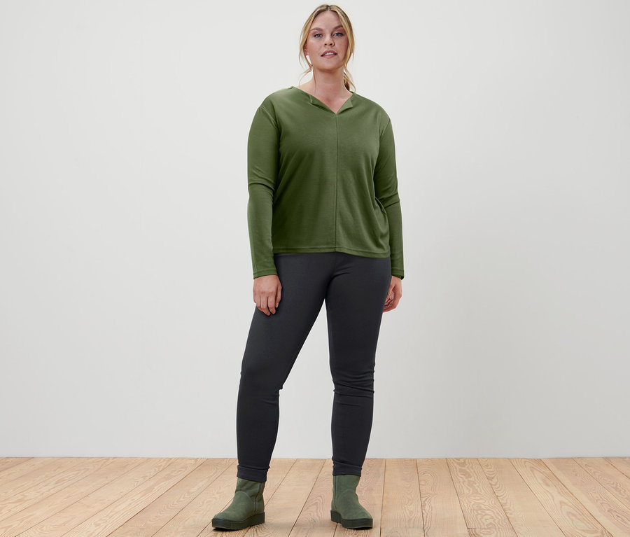 Eine Frau steht und trägt ein Blusenshirt, Jeggings und Veloursleder-Boots.