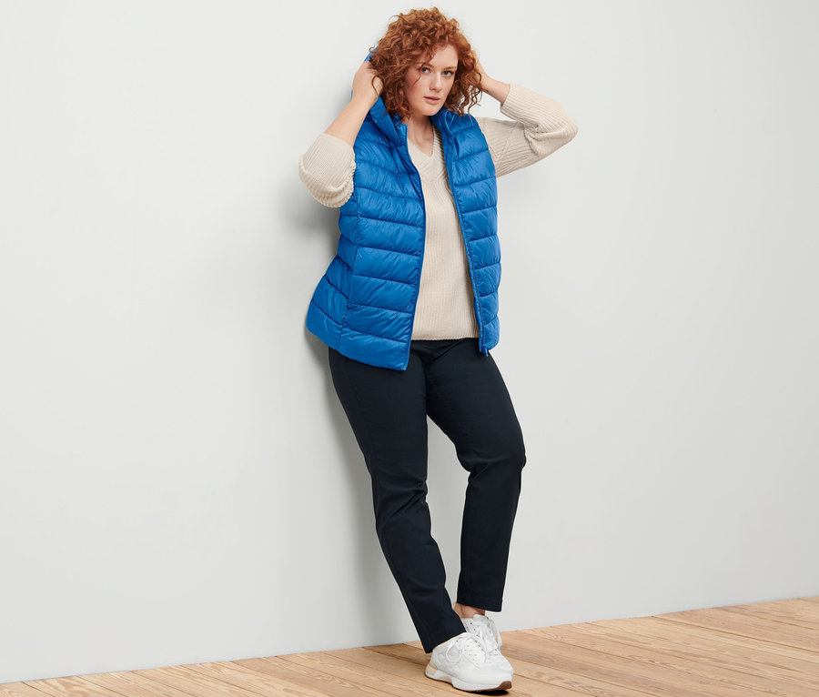 Frau posiert in Steppweste mit Kapuze, offwhite Strickpullover und dunkelblauer Bengalin-Hose.