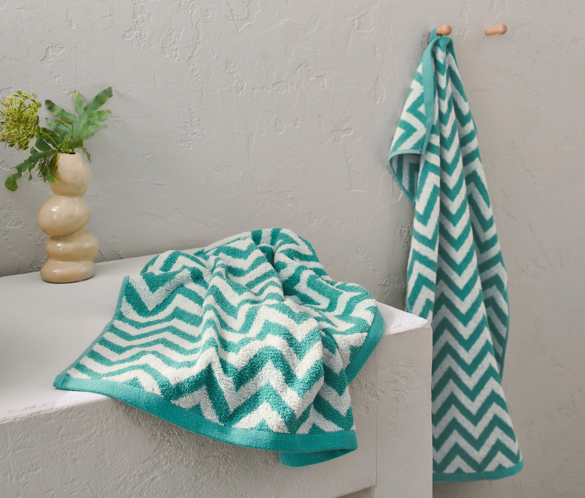 Zwei Aqua Jacquard-Handtücher liegen auf einem Waschtisch, eines hängt an einem Haken.