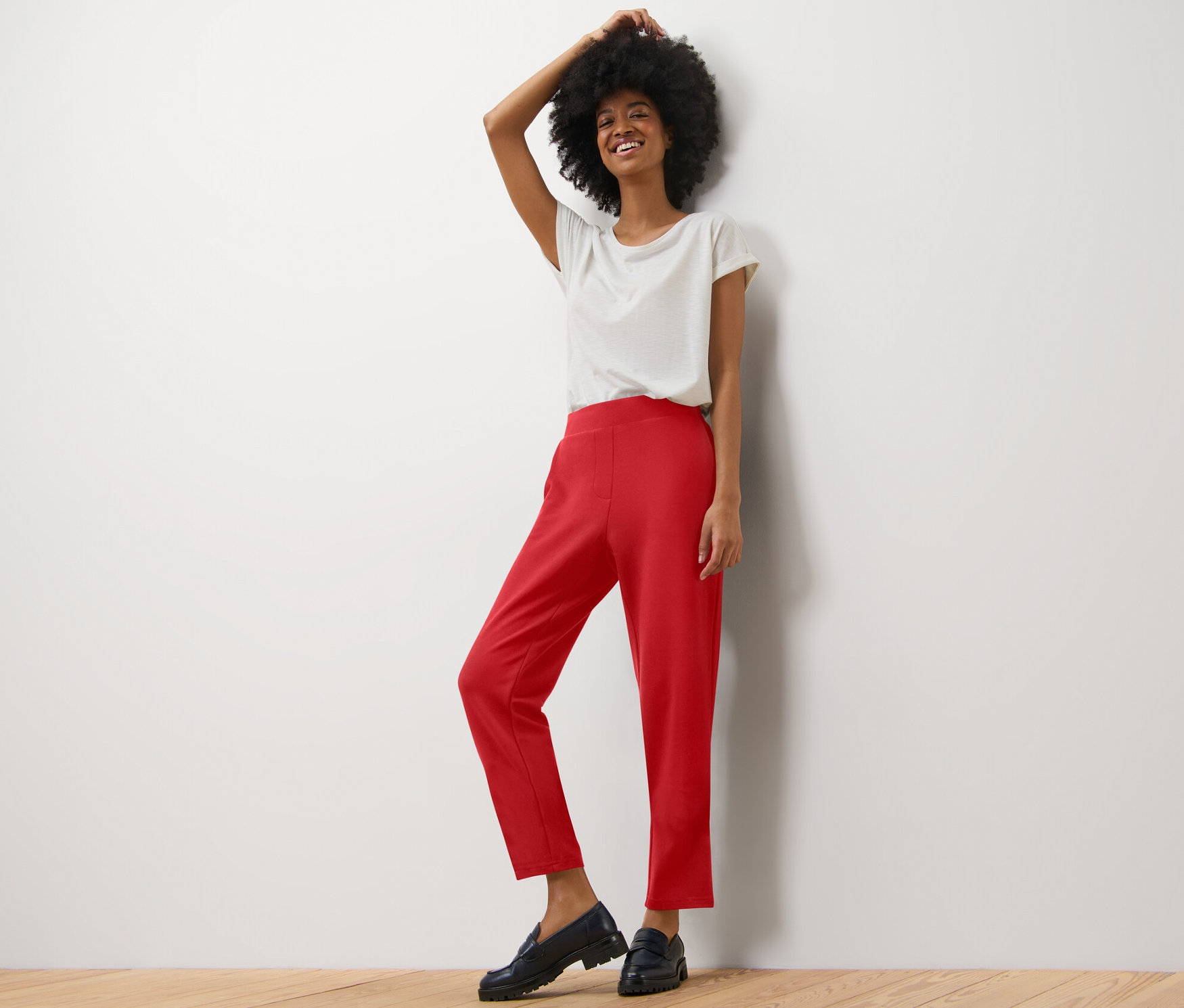 Frau posiert in hellem T-Shirt und roten Joggpants.