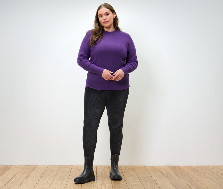 Frau posiert in Feinstrickpullover und Cord-Leggings.