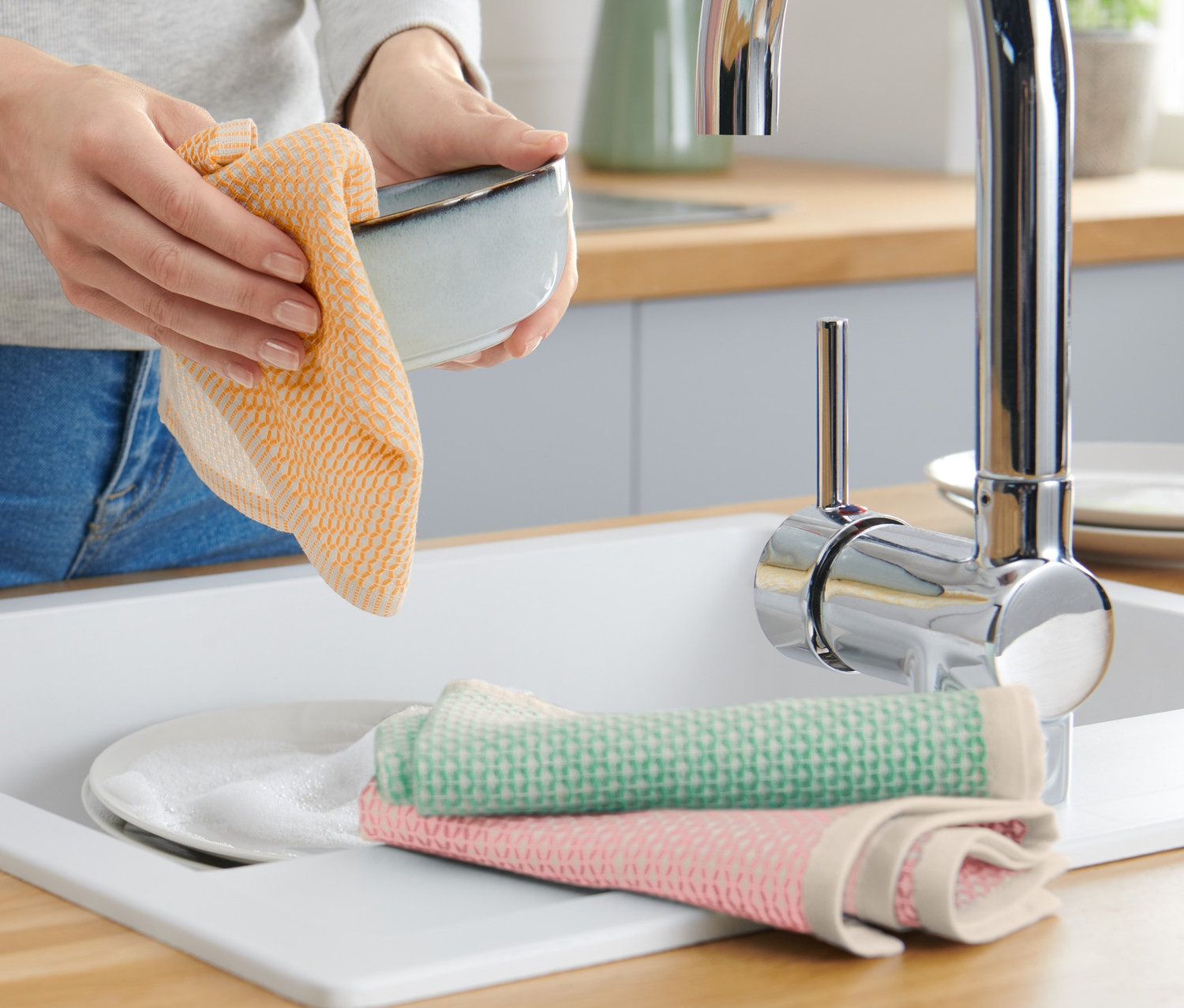 Frau trocknet Schüssel mit einem orangefarbenen 3 Spültücher.