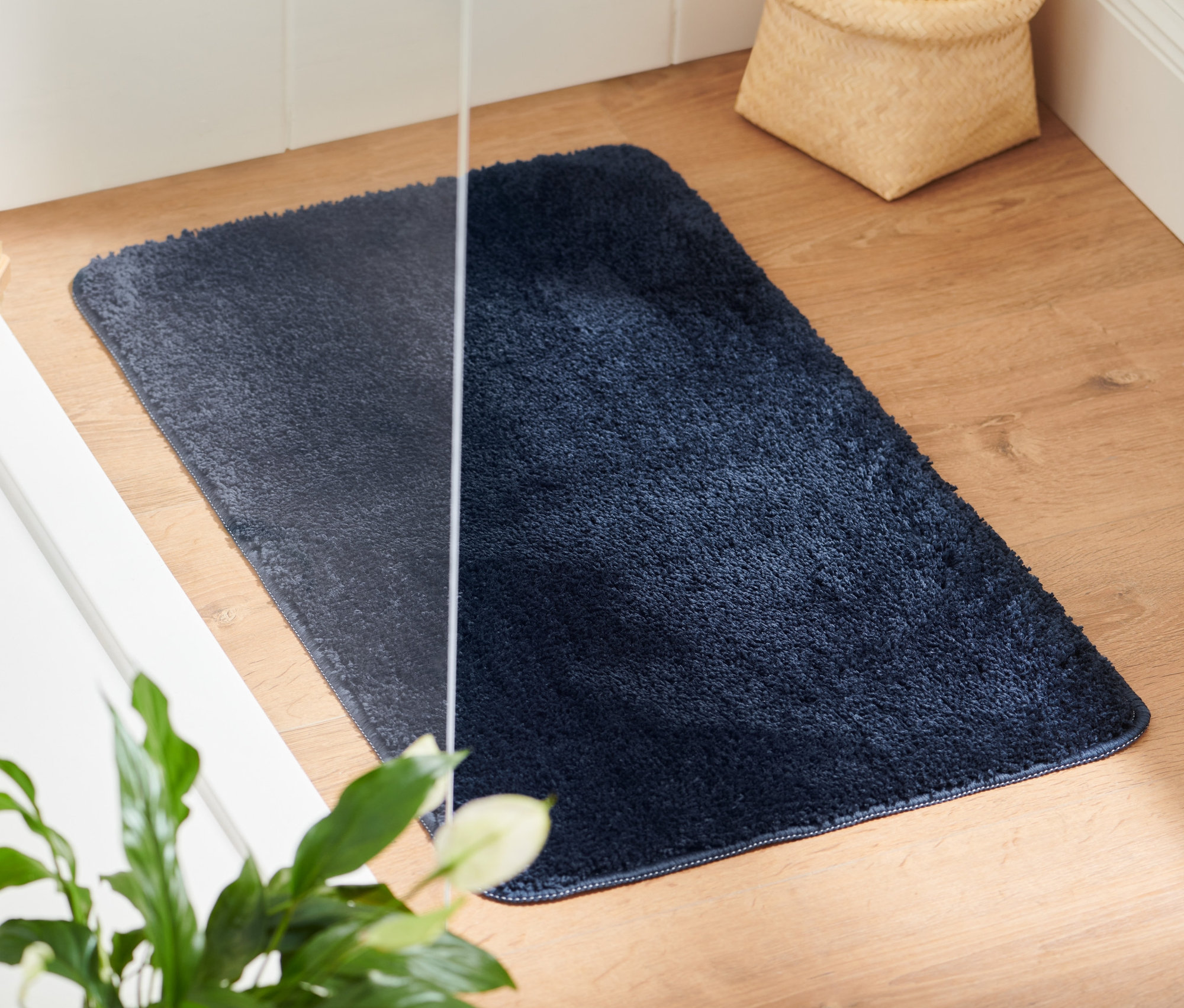 Eine blaue Badematte, ca. 45 x 75 cm, liegt auf einem Holzboden neben einer weißen Badewanne.