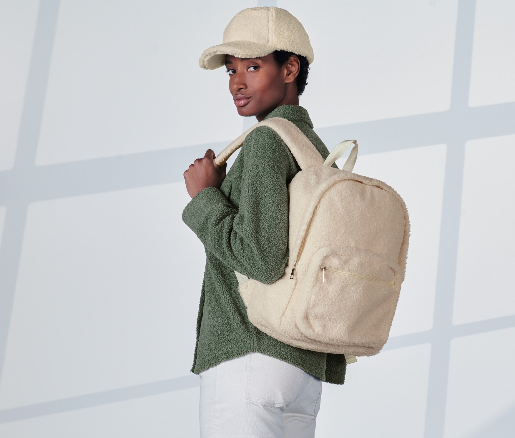 Frau mit einem cremeweißen Teddy-Rucksack und einer cremeweißen Baseballkappe.