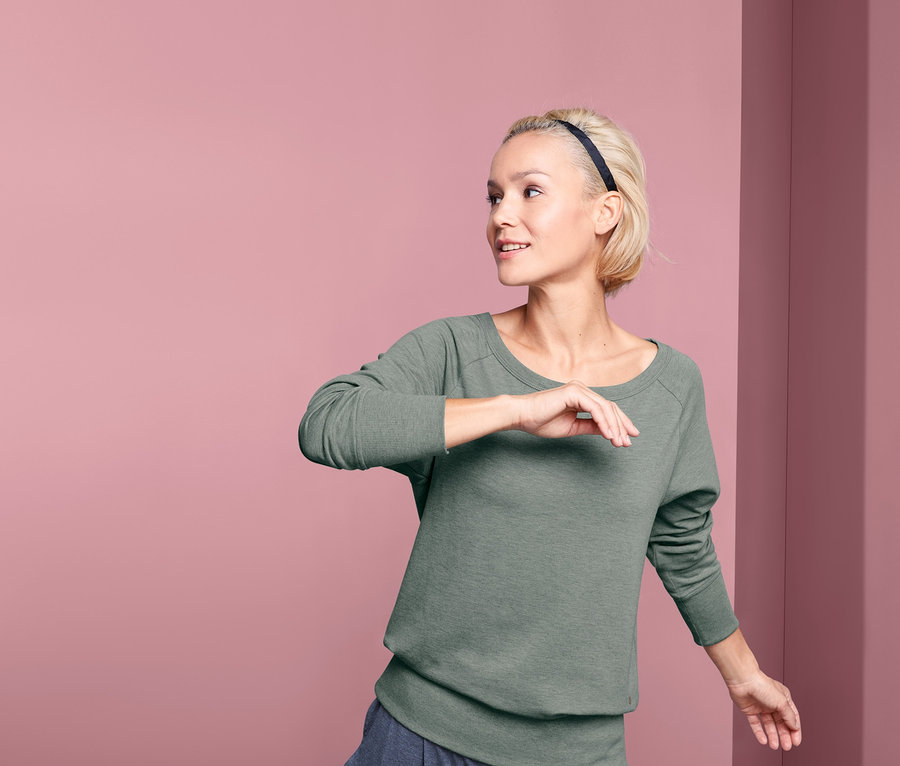 Frau im Yogasweatshirt posiert vor rosa Hintergrund.