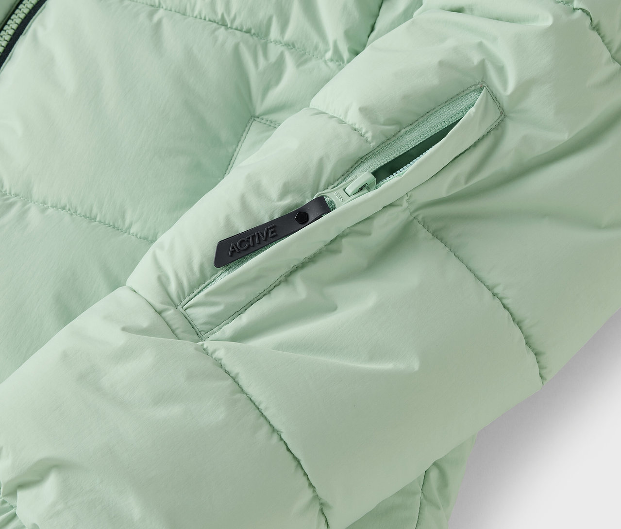 Detailaufnahme einer hellgrünen Steppjacke mit Reißverschlusstasche.