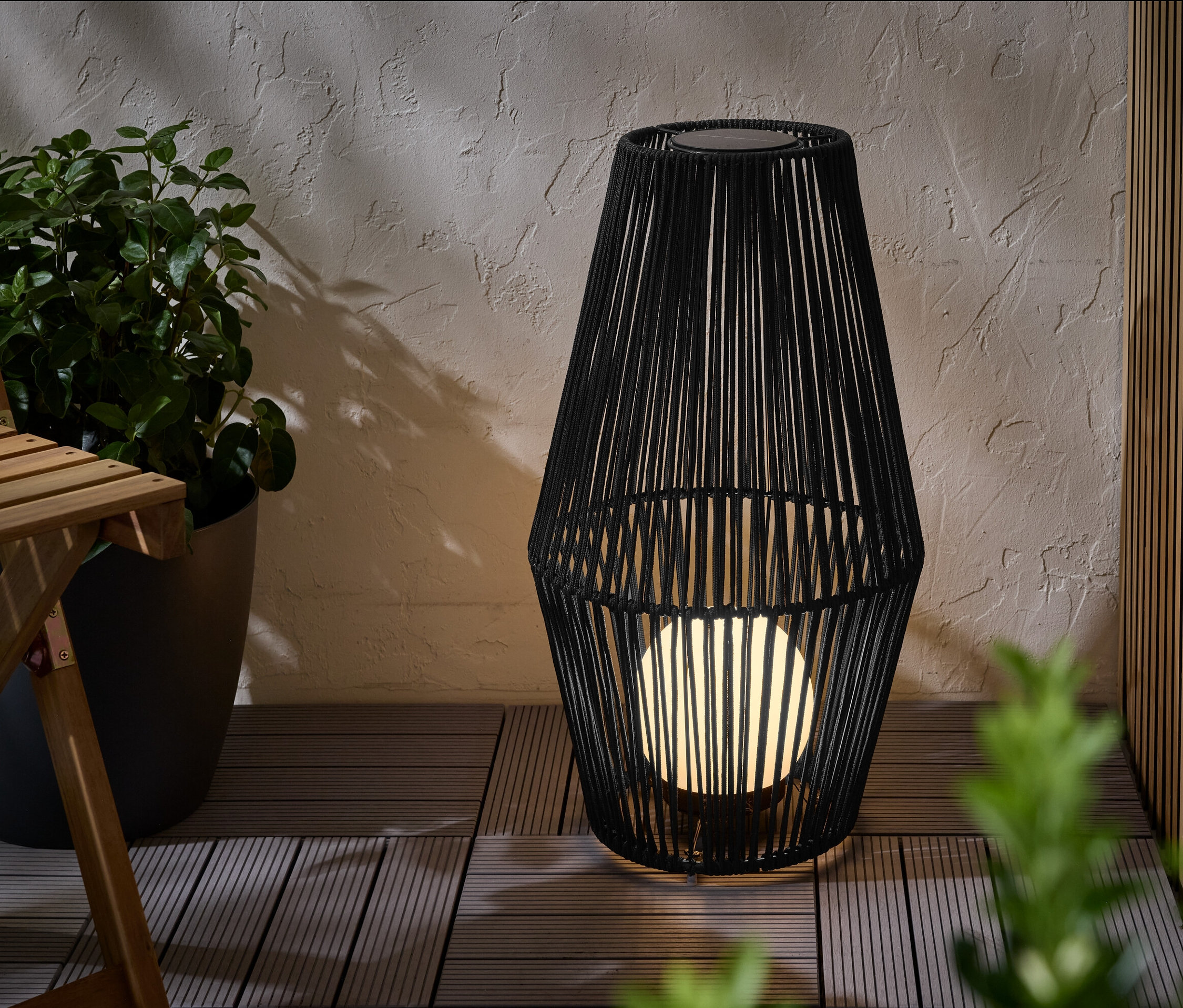 Eine große Solar-Laterne mit Textilband steht auf einer Terrasse.