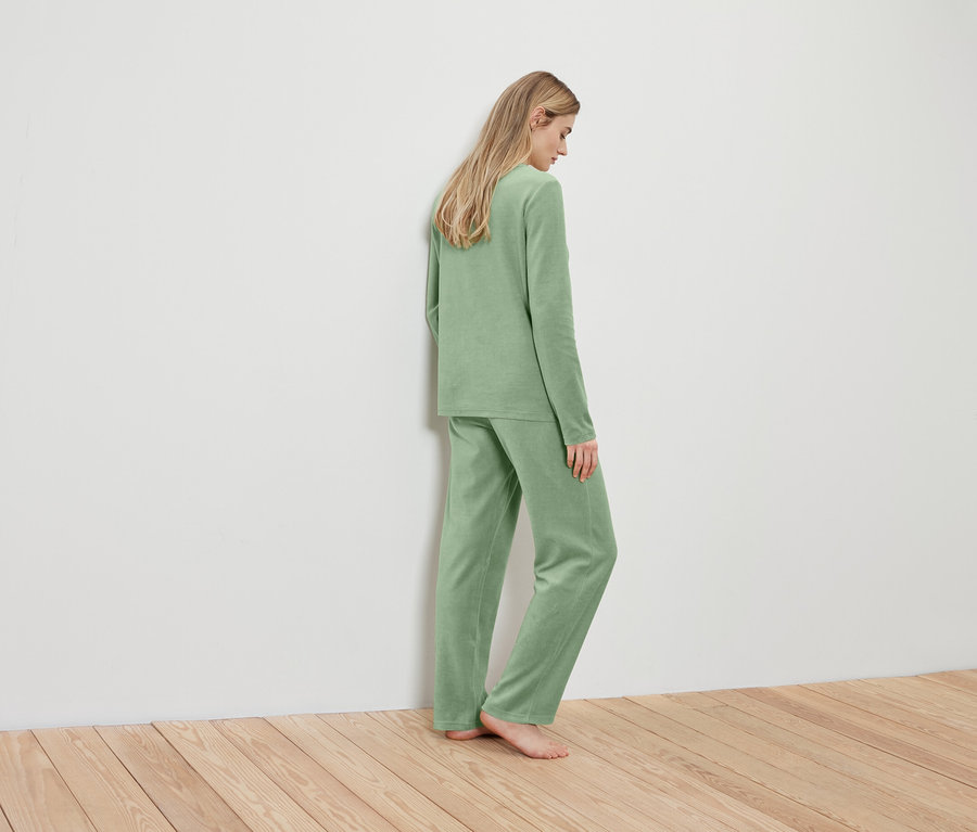Blonde Frau in hellgrünem Pyjama steht mit dem Rücken zur Wand.