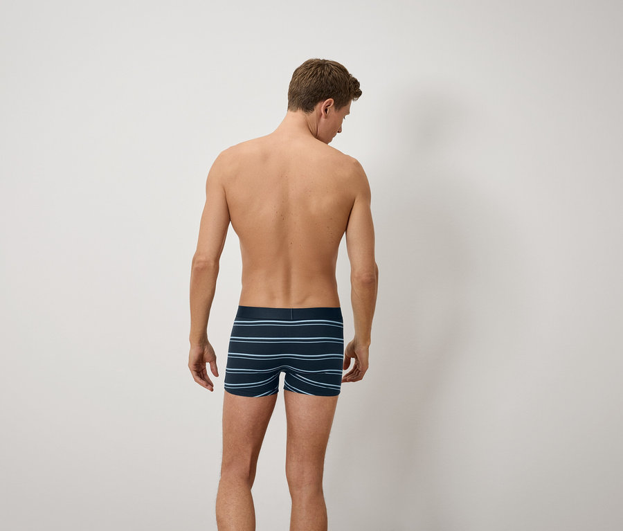 Mann mit dem Rücken zur Kamera trägt blau gestreifte Boxershorts.