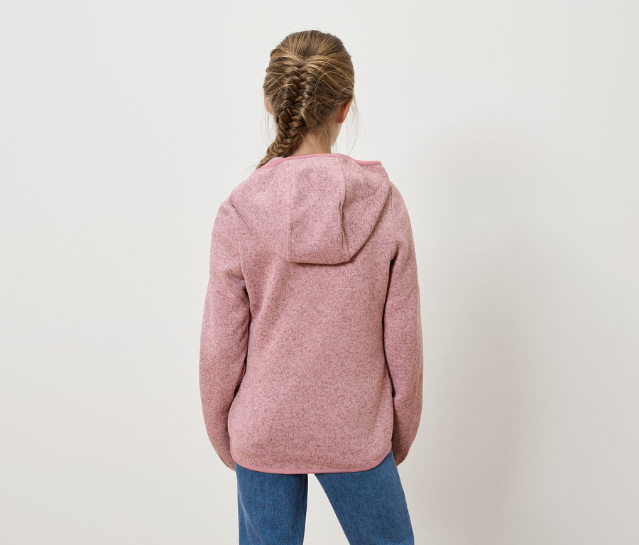 Mädchen mit Zopf steht mit dem Rücken zur Kamera und trägt einen rosafarbenen Kapuzenpullover und Jeans.