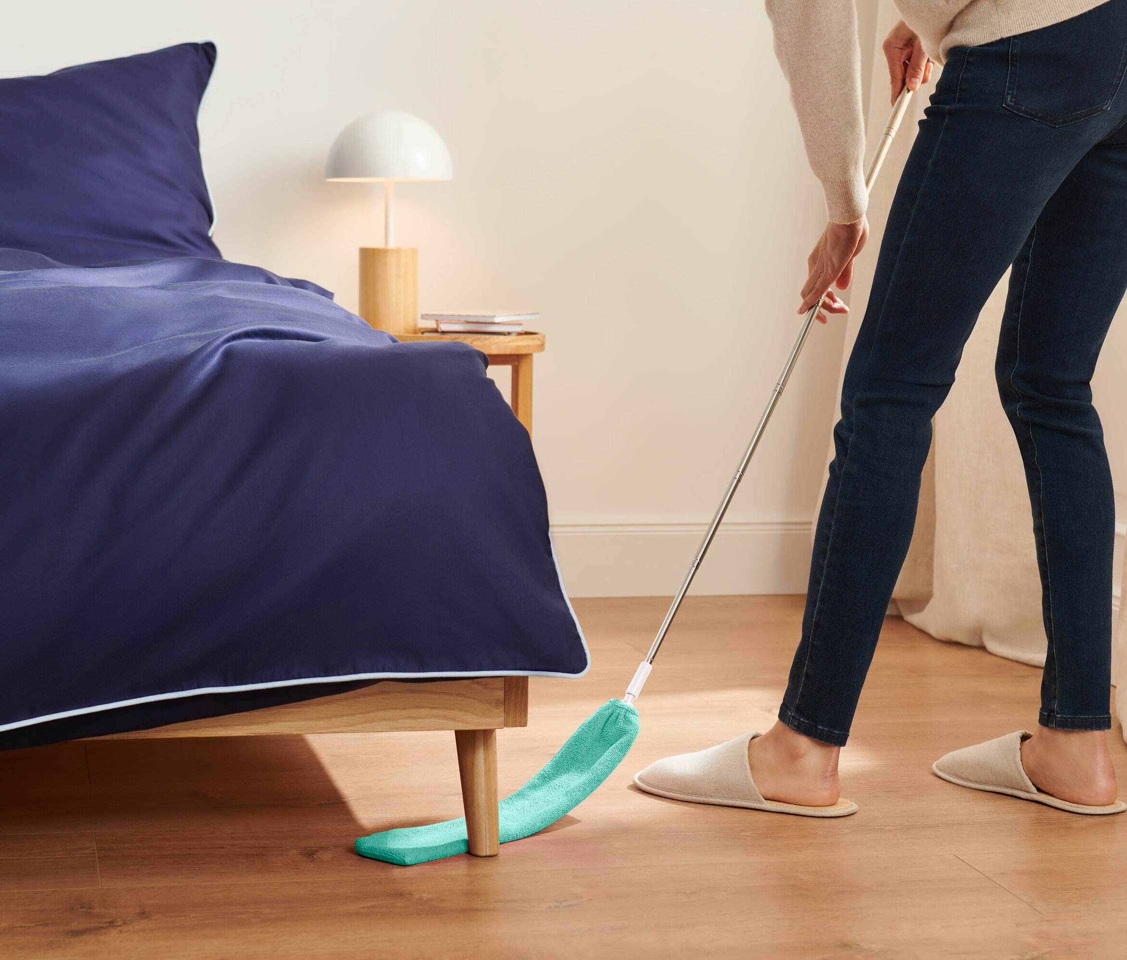 Eine Frau wischt mit einem grünen Mopp unter dem Bett.