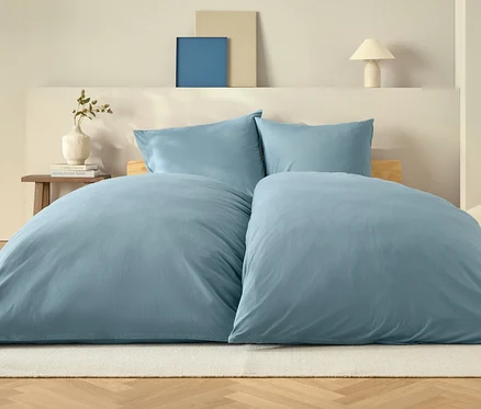 Blaue Bettdecke und zwei Kissen auf einem Bett auf einem weißen Teppich.
