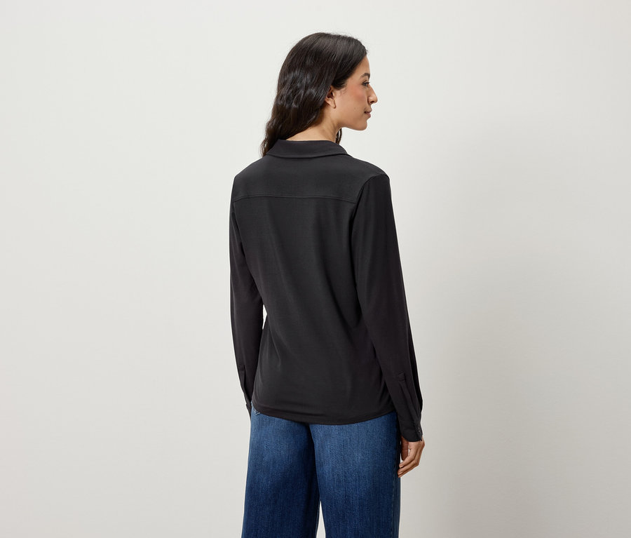 Rückansicht einer Frau mit langen Haaren in einem schwarzen Langarmhemd und blauen Jeans.