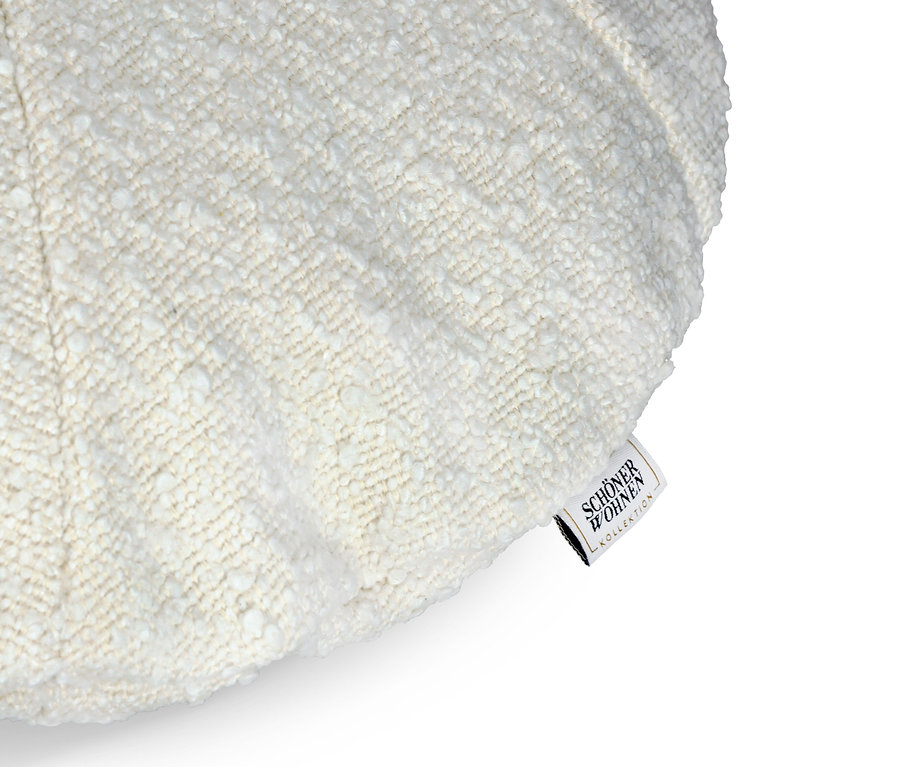 Detailaufnahme eines cremefarbenen Kissens mit sichtbarer Stofftextur und einem Etikett mit der Aufschrift SCHÖNER WOHNEN.