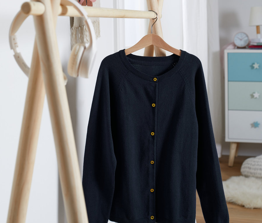 Eine blaue Strickjacke hängt an einem Kleiderbügel.