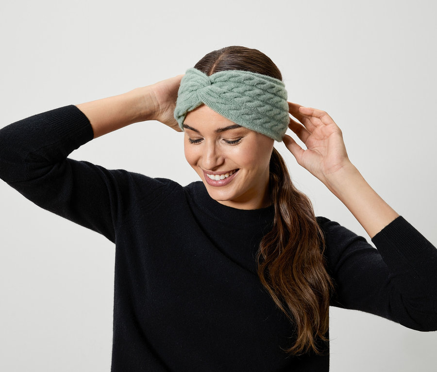Frau setzt ein hellgrünes Strick-Stirnband auf.