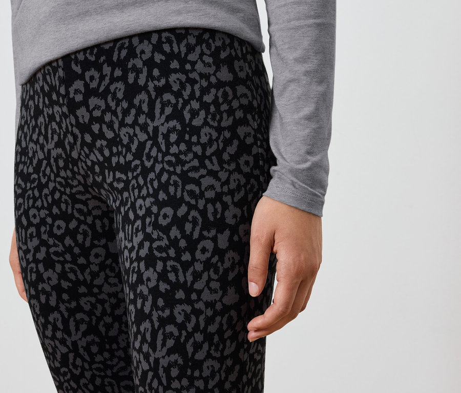 Detailaufnahme einer Person, die schwarze Leggings mit grauem Tiermuster und ein graues Langarmshirt trägt.