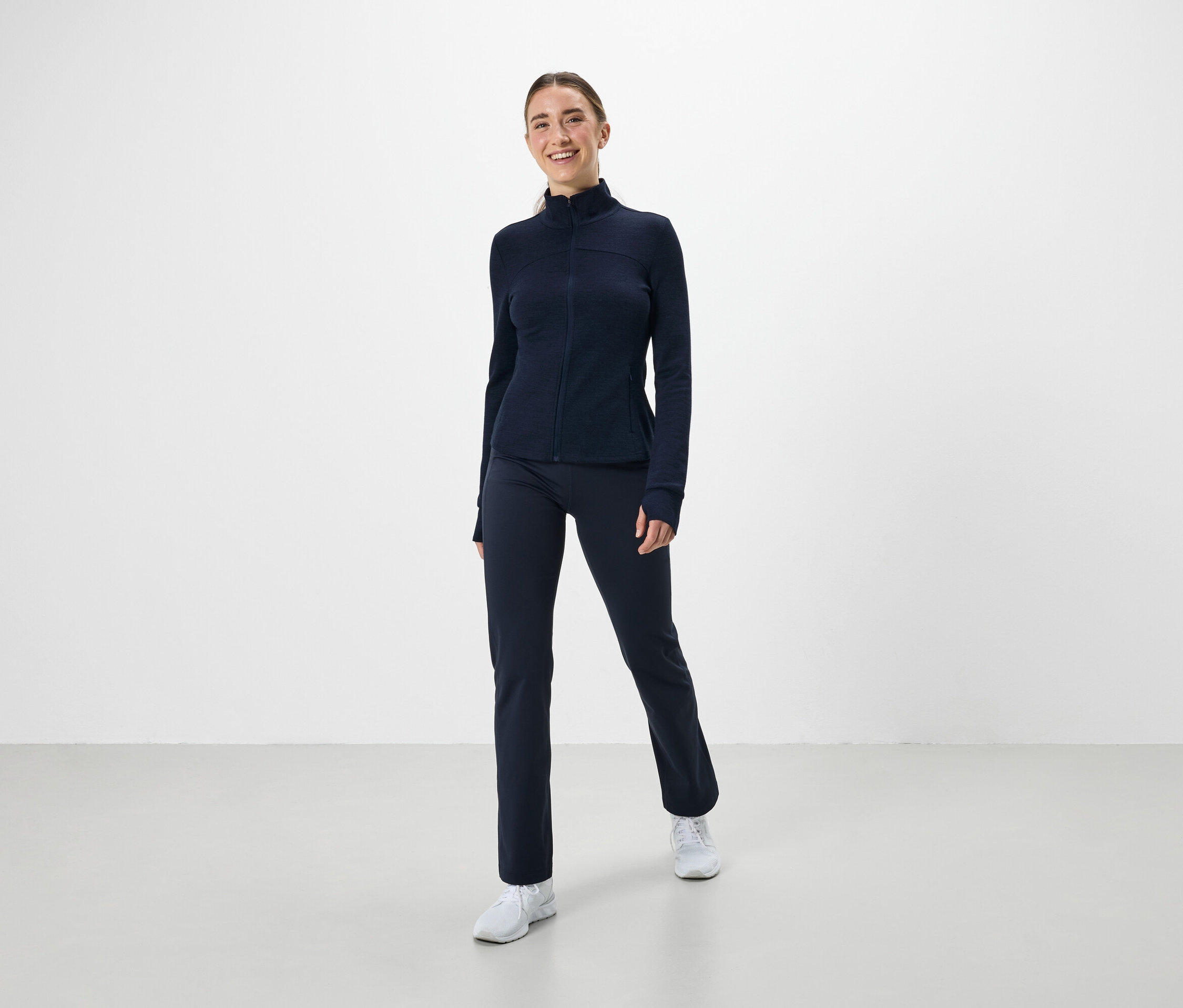 Eine Frau trägt ein marineblaues Sportoutfit und weiße Turnschuhe.