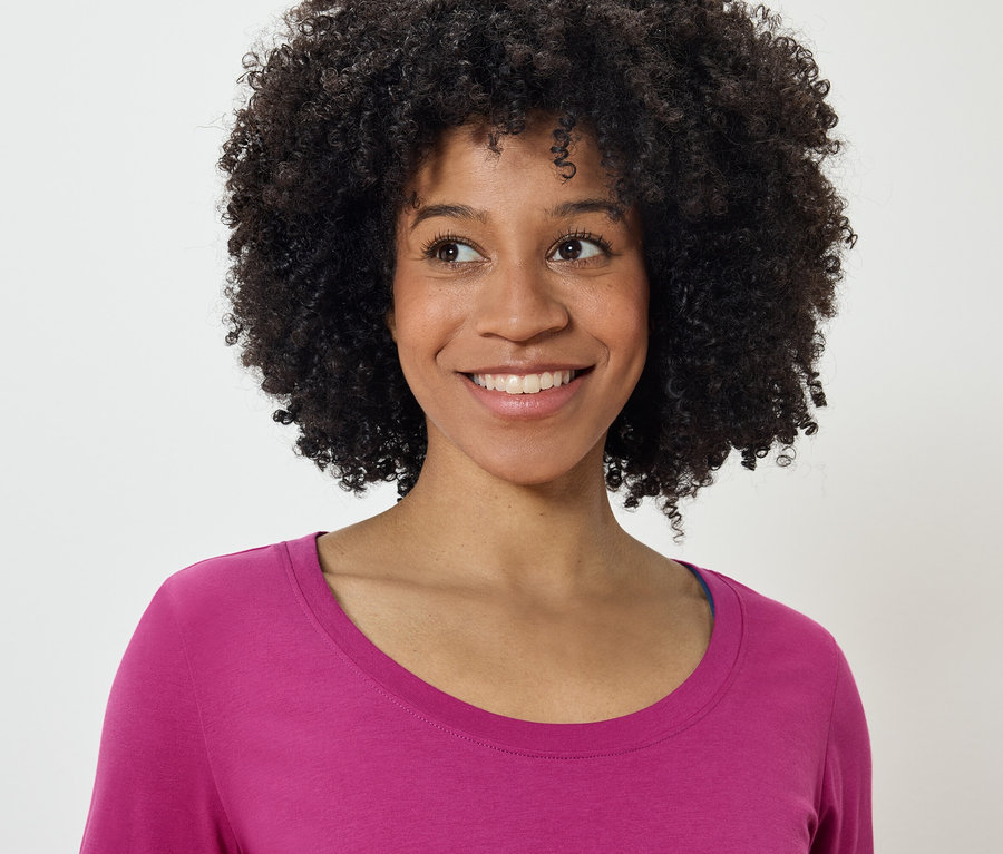 Porträt einer lächelnden Frau mit Afro-Frisur in einem pinkfarbenen T-Shirt, die nach links schaut.