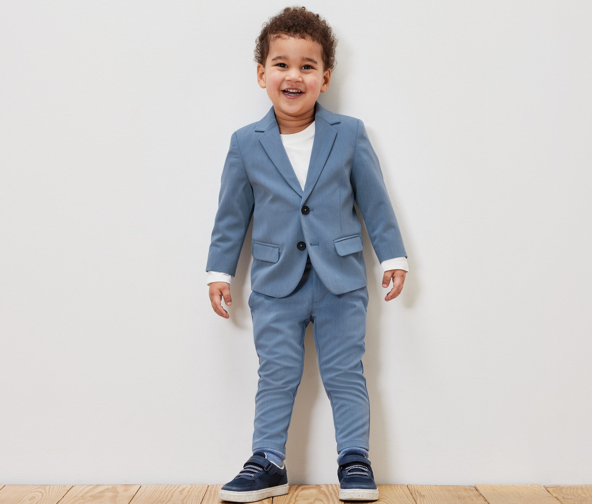 Lächelnder kleiner Junge in Kinder-Sakko und Kinder-Chinohose in Blau.